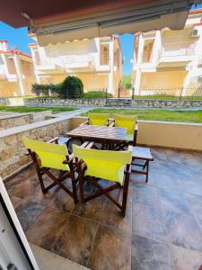 a patio with a wooden table and yellow chairs at DARIVA apartment Nea Skioni in Nea Skioni