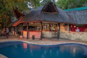 um restaurante com telhado de palha ao lado de uma piscina em The Victoria Falls Waterfront em Livingstone