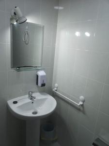 Baño blanco con lavabo y espejo en Hostal Conde de Lemos en Ponferrada