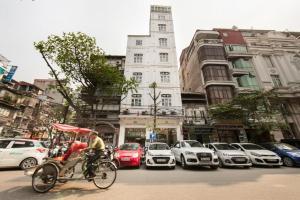 um homem a andar de bicicleta numa rua movimentada da cidade com carros em Serenity Diamond Hotel 1E Cửa Đông - by Bay Luxury em Hanói