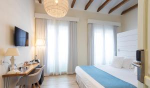 Habitación de hotel con cama, escritorio y TV. en Madeinterranea Suites en Málaga