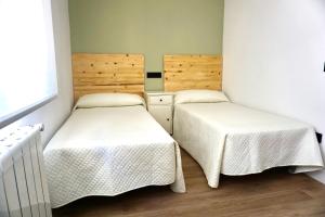 2 bedden in een kleine kamer met witte lakens bij Casa El Acebal in Llanes