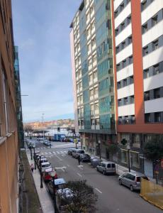 une rue de la ville avec des voitures garées et un grand bâtiment dans l'établissement Piso playa Gijon, à Gijón