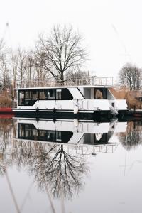 德米茨Deine schwimmende Auszeit auf dem Wasser -Festlieger Hausboot Tobago的船停靠在河上,倒映在河里
