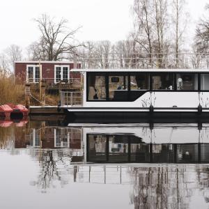 德米茨Deine schwimmende Auszeit auf dem Wasser -Festlieger Hausboot Tobago的水面上的船,有房子的背景