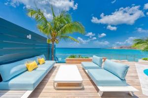 a patio with blue couches and a palm tree and the ocean at Surfsong Villa- Luxury Water Front Villa for 12 in Maho Reef