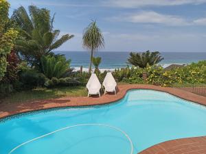 a swimming pool with two chairs and the ocean at Whispering Waves in Bazley Beach
