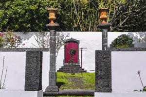 uma porta vermelha numa parede branca com uma cerca em Quinta dos Mistérios- Turismo de Habitação em Fajã de Santo Amaro