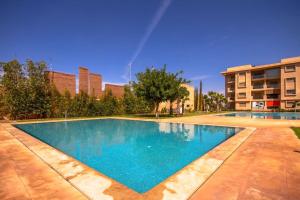 a large swimming pool with blue water in front of a building at Appartement luxueux Coralia avec piscine in Marrakech