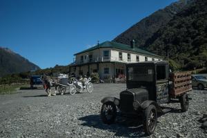 um carro velho e uma carruagem puxada a cavalo em frente a uma casa em Otira Stagecoach Hotel em Otira