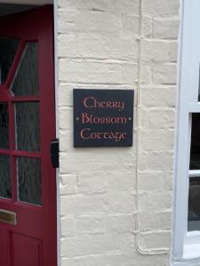 een bord aan de zijkant van een gebouw met een rode deur bij Cherry Blossom Cottage ,4 Cherry Street , Old Town ,Stratford Upon Avon in Shottery