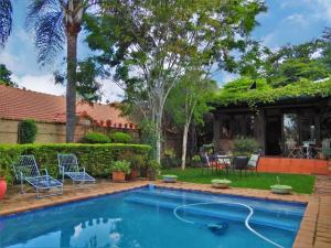 a swimming pool in a yard with chairs and a house at Ambiance Guesthouse in Pretoria