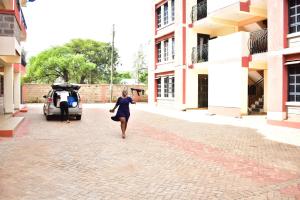 Eine Frau, die eine Straße entlang läuft, neben einem Fahrzeug. in der Unterkunft Bomani Penthouse in Kisumu