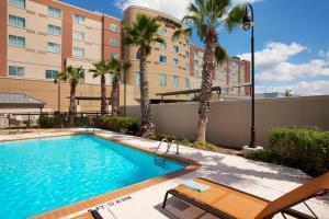 a swimming pool with palm trees and a building at Courtyard Marriott Houston Pearland in Pearland