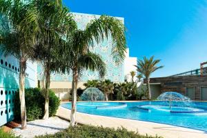 a swimming pool with palm trees in front of a building at Le Meridien Oran Hotel in Oran