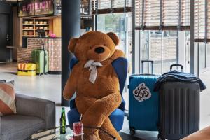 a large brown teddy bear sitting in a chair with suitcases at Moxy Amiens in Amiens