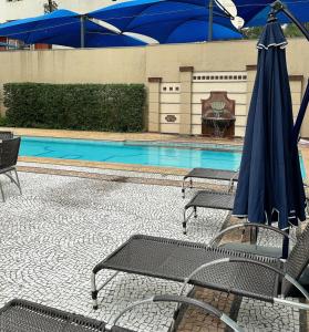 a pool with chairs and a blue umbrella at Sao Paulo Ibirapuera Privilege - Suite Deluxe in Sao Paulo