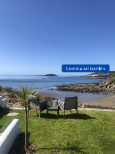 two benches sitting on the grass near a beach at Ocean View Apartments in Looe