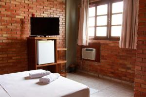 1 dormitorio con 1 cama, TV y pared de ladrillo en Rede Andrade Goiania Centro, en Goiânia
