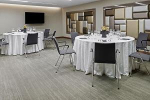AC Hotel by Marriott Panama City في مدينة باناما: قاعة اجتماعات مع طاولات وكراسي بيضاء وتلفزيون بشاشة مسطحة