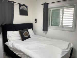 un lit blanc avec une tête de lit noire et une fenêtre dans l'établissement דירת סטודיו יפיפיה על גג ומרפסת שמש ברחוב הירקון, à Tel Aviv