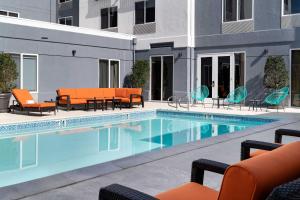 una piscina con sillas naranjas y sillas junto a un edificio en Aloft Mountain View, en Mountain View