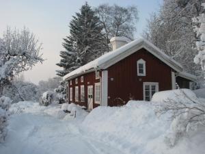 una casa roja cubierta de nieve con árboles en el fondo en Lillåns B&B, en Örebro