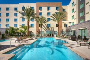 a pool with chairs and palm trees in front of a hotel at Courtyard by Marriott Los Angeles LAX/Hawthorne in Hawthorne