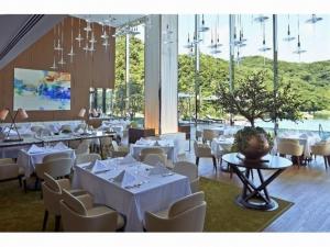 西海市にあるオリーブベイホテルの白いテーブルと椅子、大きな窓のあるレストラン