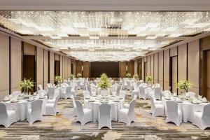 une salle de banquet avec des tables et des chaises blanches ainsi qu'un lustre dans l'établissement Courtyard by Marriott Chengdu South, à Chengdu