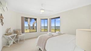 a white bedroom with windows and a bed and a chair at Sea Cottage - Beachside Paradise in Beachmere