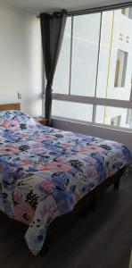 a bed with a colorful comforter in a room with a window at apartamento Lynch Costero Iquique in Iquique