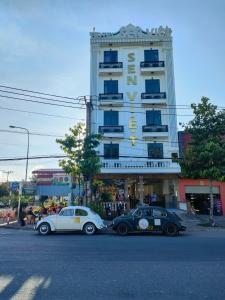 dos autos están estacionados frente a un edificio en Hotel Sen Việt Bạc Liêu, en Bạc Liêu