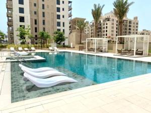 a large swimming pool with white chairs and buildings at Dar Vacation - Modern Luxury 1BR Apartment in MJL in Dubai