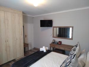 Dormitorio con cama, escritorio y TV en Blue Owl Guest House, en Mossel Bay