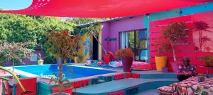 a woman sitting under a red umbrella next to a house at Cape Agulhas BACKPACKERS in Struisbaai