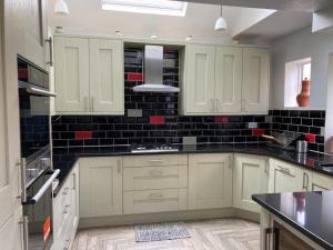 a kitchen with white cabinets and black tiles on the wall at Guildford Home - Free Parkings, River, Waterfall View & Woodland Garden, Guildford, Surrey, UK in Bramley