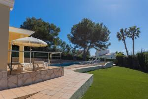 een patio met stoelen en een parasol naast een zwembad bij Villa Llebeig 155TS Son Bou By MENORCARENTALS in Son Bou