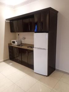 een keuken met een witte koelkast en zwarte kasten bij Nawara Hotel in Riyad