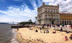 un groupe de personnes assises sur la plage en face d'un bâtiment dans l'établissement Romantic Nest for a Getaway with Design & Free Parking, à Lisbonne