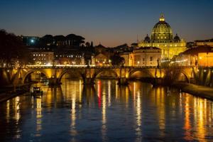a bridge over a river with a city at night at Colosseo Ohana Suite in Rome