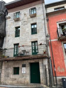 um edifício de pedra com uma varanda e portas verdes em Apartamentos El Escudo Centro em Ribadesella
