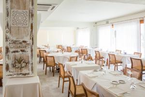uma sala de jantar com mesas e cadeiras brancas e janelas em Club Hotel Olivi - Tennis Center em Malcesine