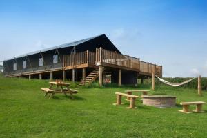 a building with a deck and picnic tables in the grass at Troney Valley Escapes - Owl's Den in Crediton