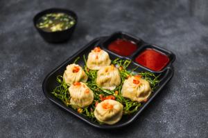 a black plate of dumplings with sauce on a table at THE Pi HOTEL IMPHAL MANIPUR in Imphal