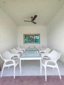 a white dining room with white chairs and a ceiling fan at Aloha Farm & Camp in Udaipur