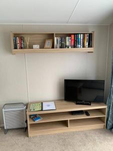 uma sala de estar com televisão e uma prateleira com livros em Kellysholidayhomes NEW Malton 3 bedroom Caravan em Weeley