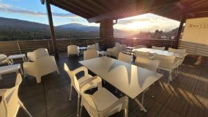 a balcony with white tables and chairs and the sunset at BayVista, die Bayerwald Lodge in Lam