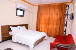 um quarto com uma cama e uma cadeira vermelha em Hotel Brahmand em Jejūri