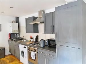 Lovely 2-bedroom serviced apartment Greater London في لندن: مطبخ مع دواليب رمادية وغسالة ومجفف